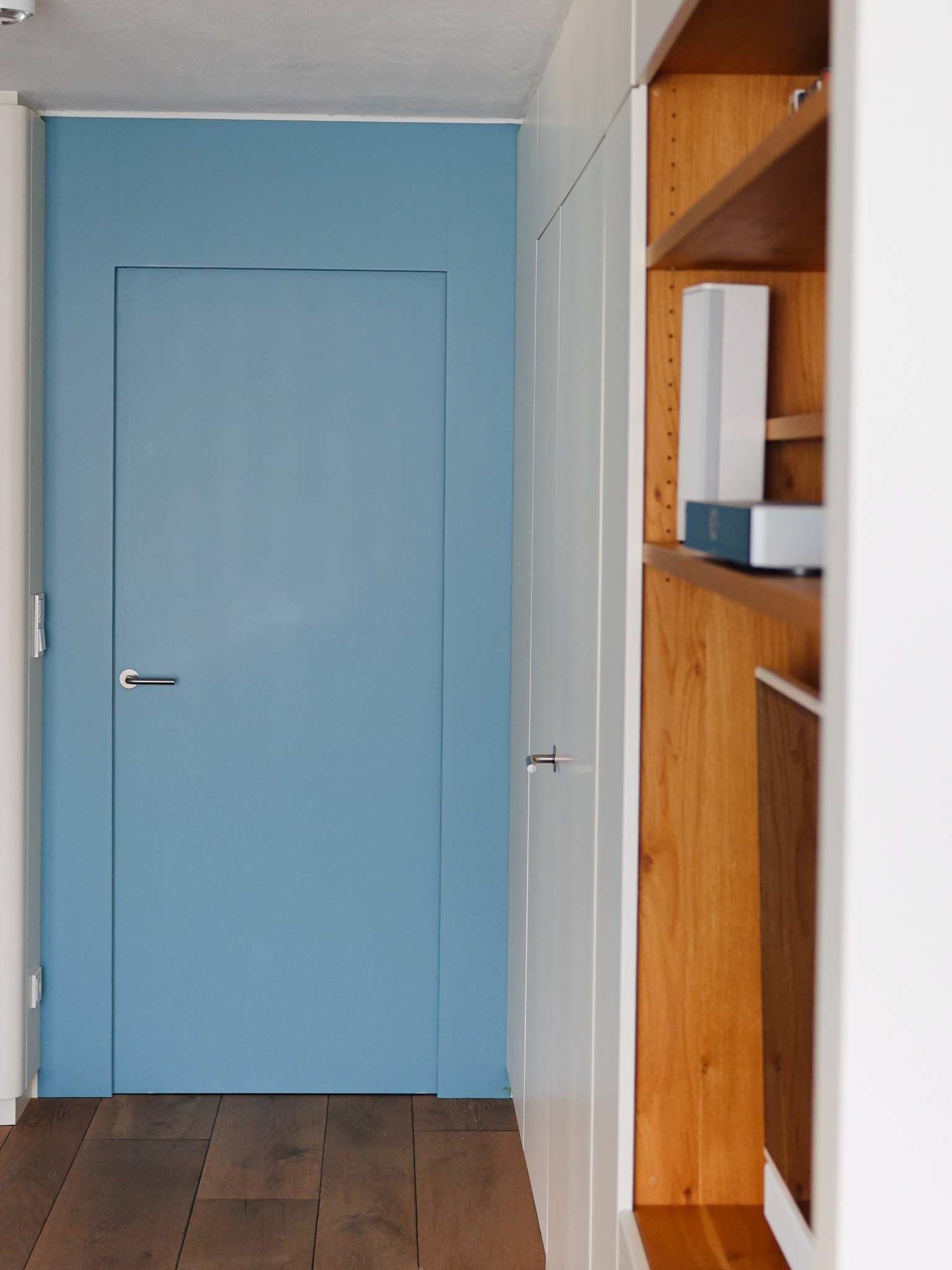 Blaue Tür zwischen weißen Einbauten und Holzregal