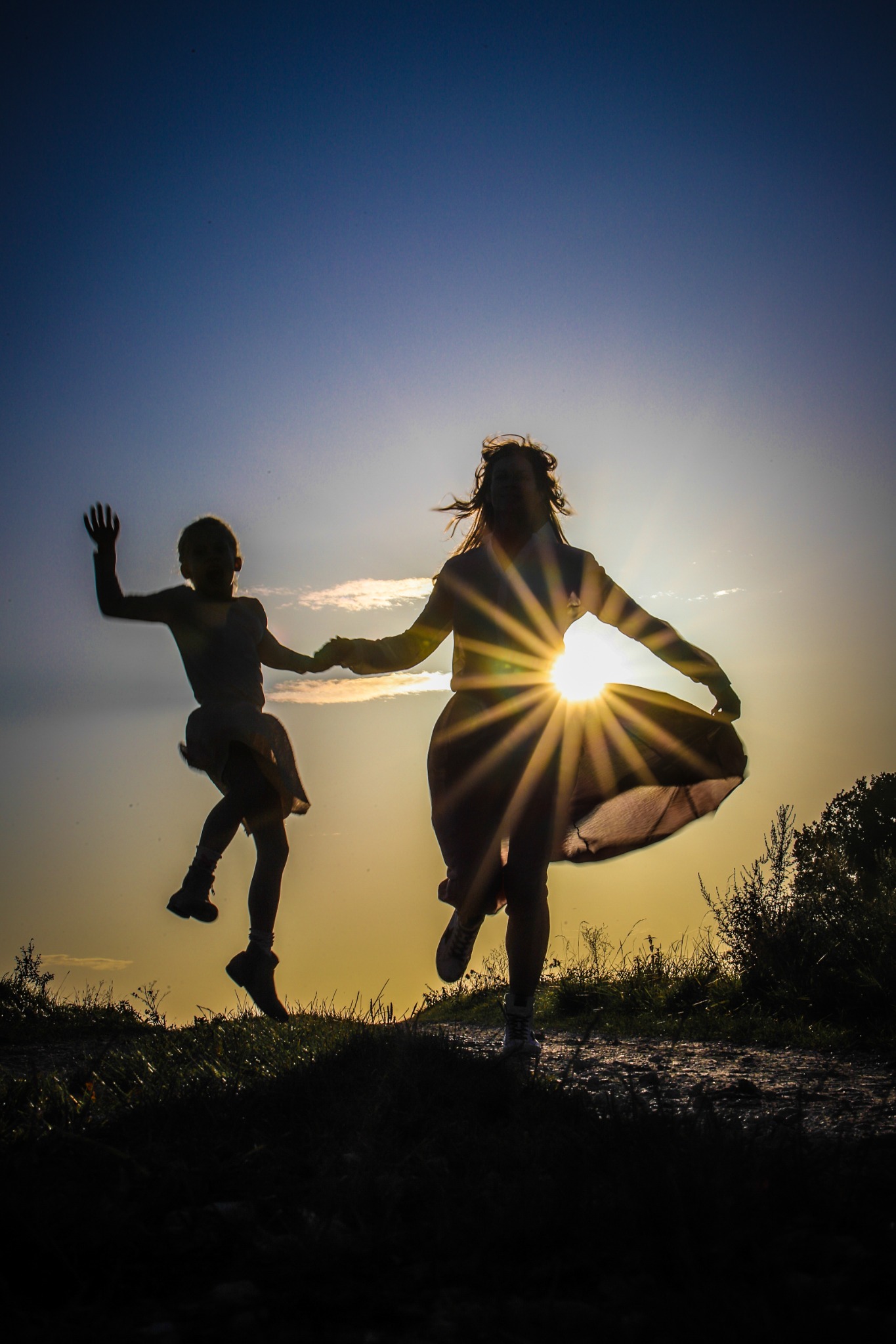 Mutter und Tochter springen als Silhouetten im Sonnenlicht