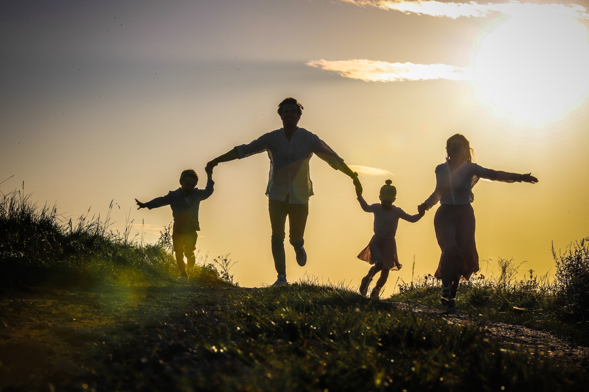 Familie springt gemeinsam als Silhouette im Abendlicht