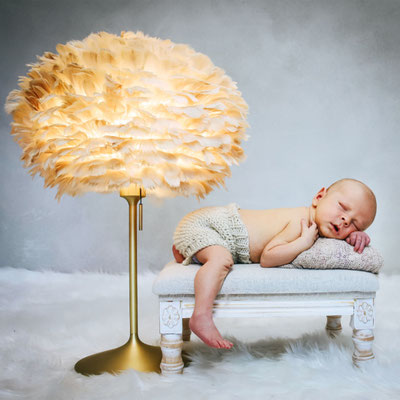 Neugeborenes Baby liegt neben einer leuchtenden Federlampe auf einer kleinen Bank