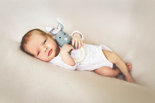 Waches Baby liegt mit einem gestrickten Kuscheltier auf einer weichen Decke